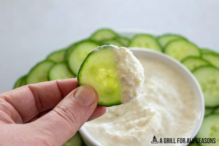hand holding a cucumber with smoked onion dip