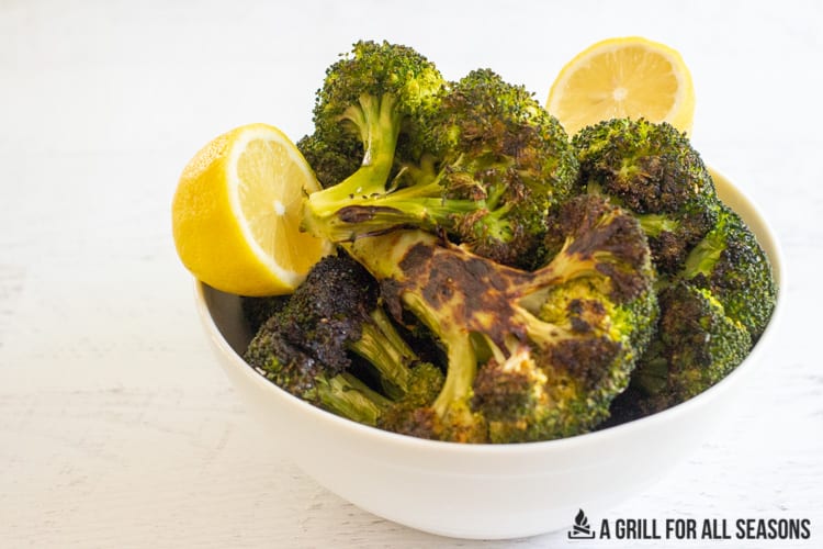 grilled broccoli in a bowl with lemon wedges