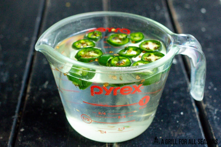 measuring cup with simple syrup and jalapeno slices