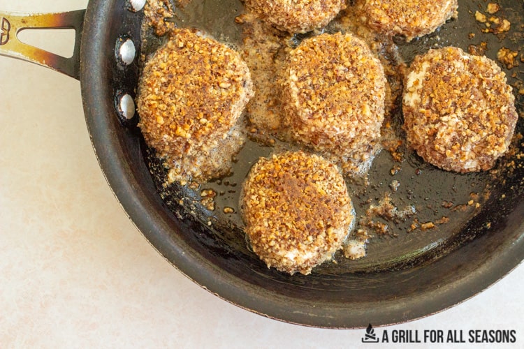 pecan crusted goat cheese being cooking in butter in a frying pan