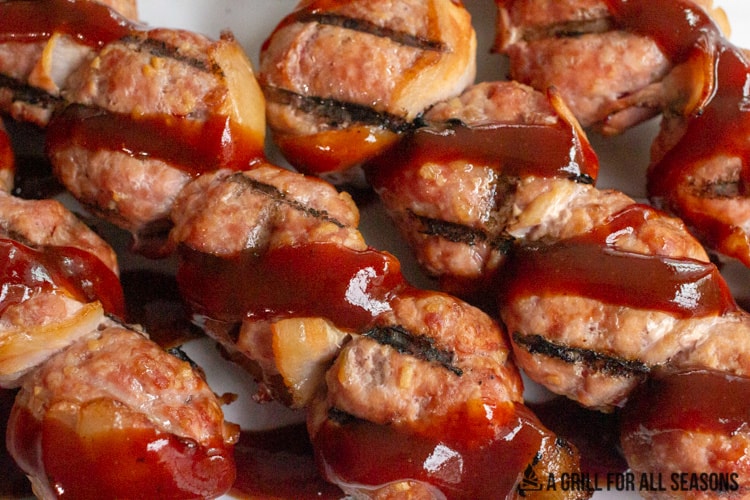 close up of 4 skewers of cooked ground pork balls with grill lines drizzled with bbq sauce
