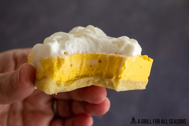 hand holding one of the one of the No Bake Mango Cheesecake Bars with a bite missing
