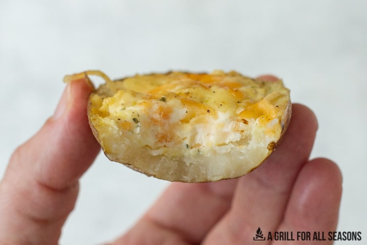 hand holding one of the smoked cheesy potatoes with a bite missing