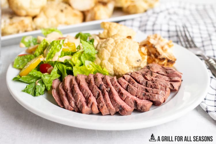 sliced smoked sirloin steak with a side salad and smoked cauliflower on a plate
