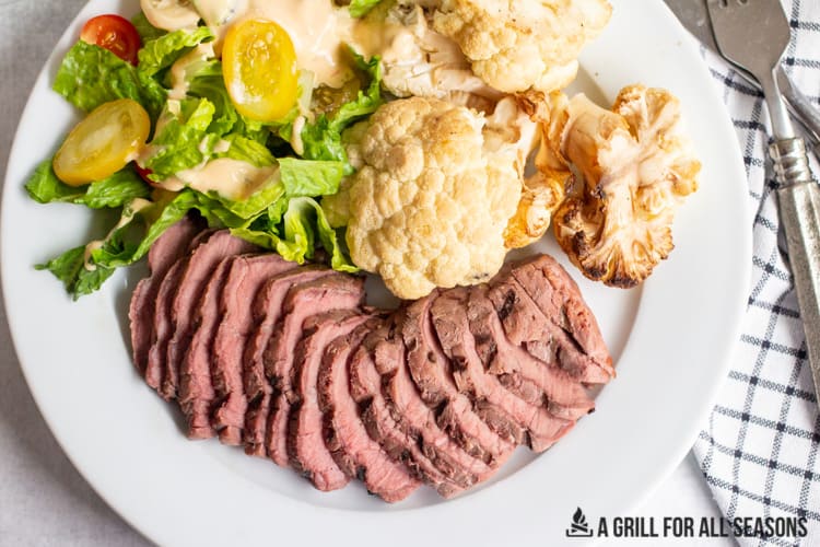 sliced smoked sirloin steak with a side salad and smoked cauliflower on a plate