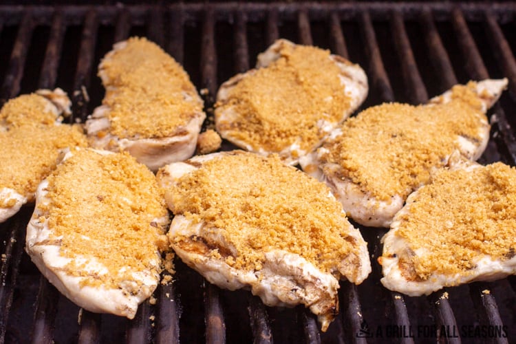 gilled chicken breasts on grill with tomato sauce, topped with pork rind crumbs