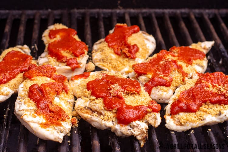 grilled chicke breasts on grill topped with tomato sauce