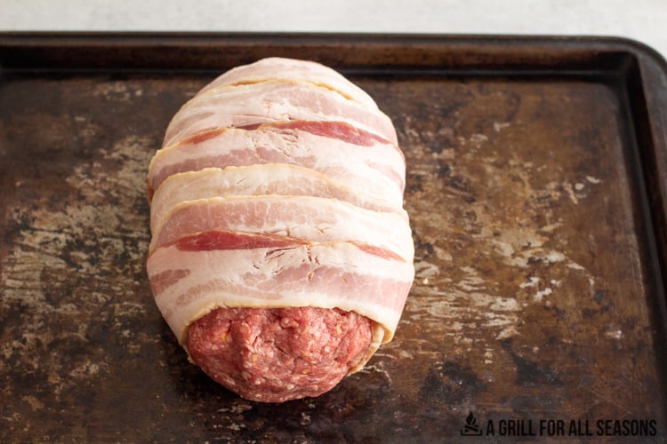 raw, uncooked meatloaf wrapped in bacon sitting on a cooking sheet.