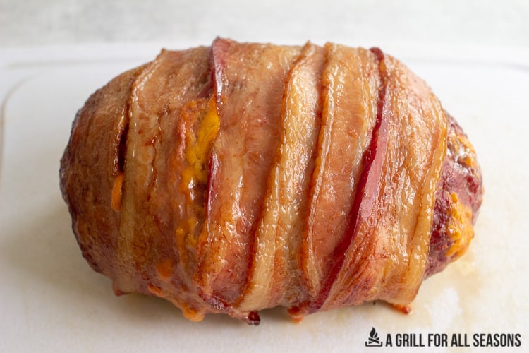 cooked meat wrapped in bacon resting on cutting board.