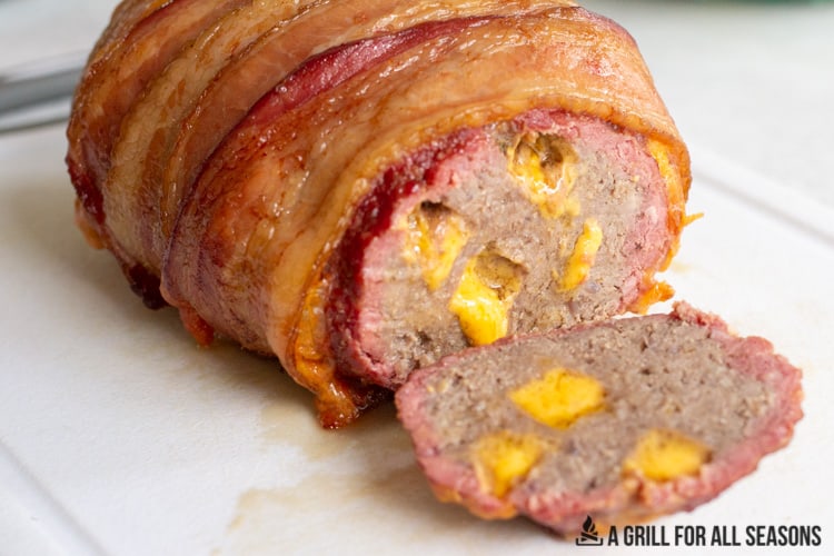 sliced view of smoked meatloaf with bacon wrapped outside and gooey cheese on the inside.
