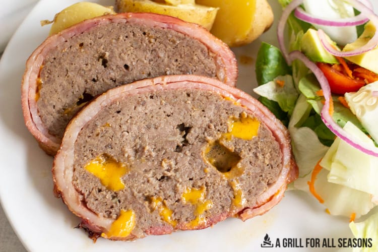 slices of smoked meatloaf on a plate with potatoes and side salad.