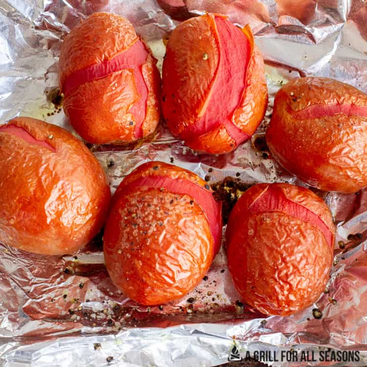 Smoked plum tomatoes with charred cracked skin on foil.