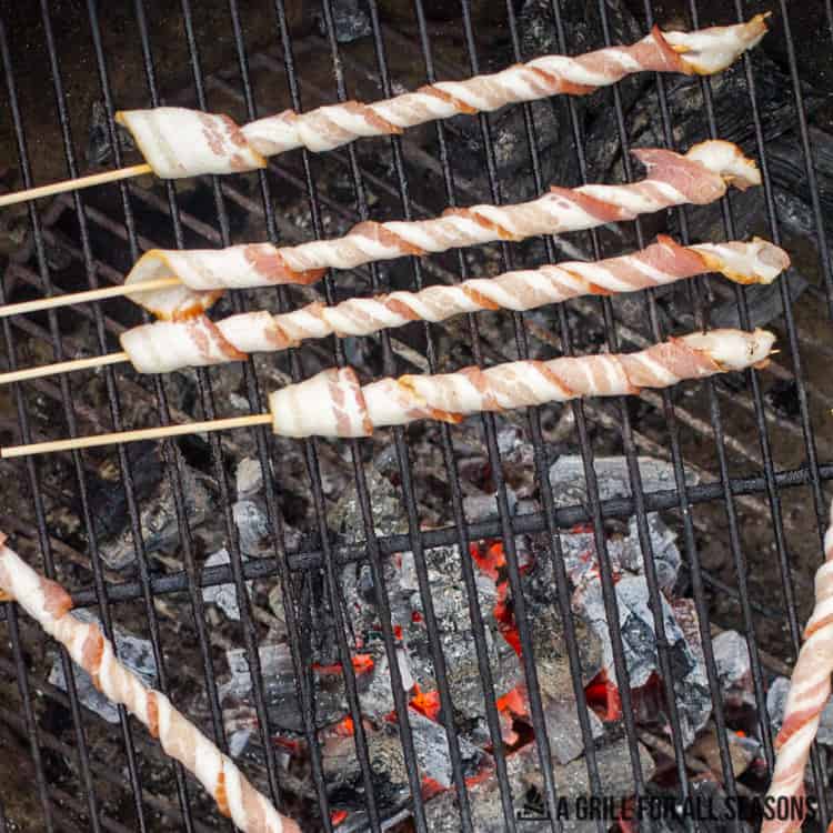 Bacon skewers sitting on a grill with hot goals.
