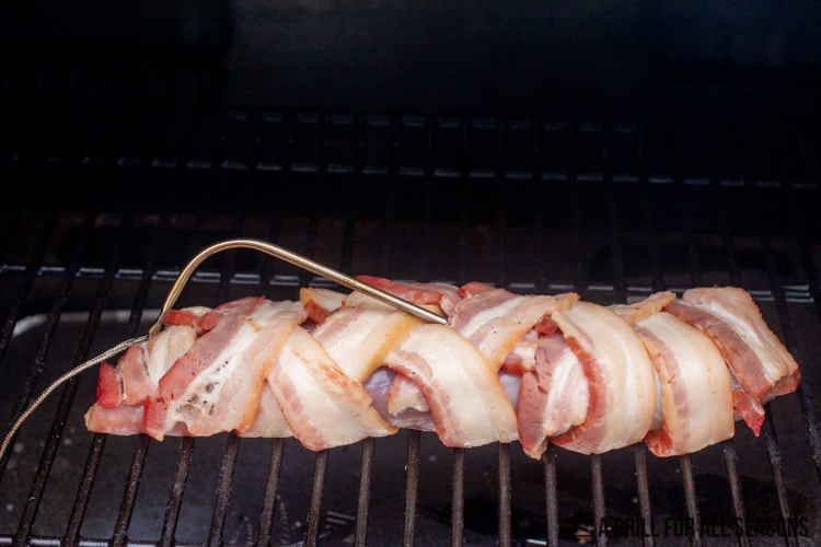 Pork tenderloin wrapped in bacon on grill being smoked.