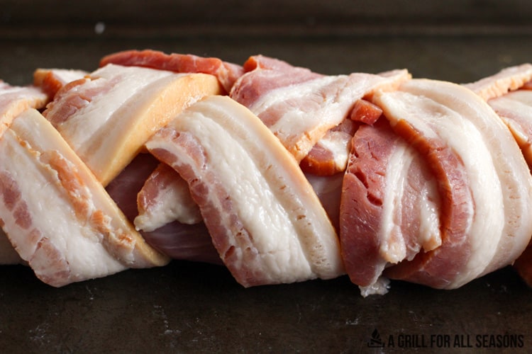 Close up of the pork tenderloin wrapped in bacon on cooking sheet.