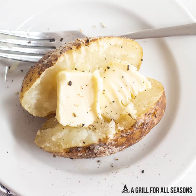 one of the traeger baked potatoes cut in half on a plate with butter salt and pepper