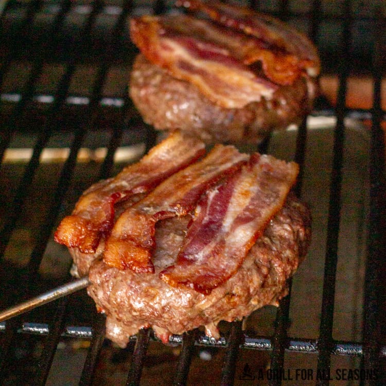 Burgers on smoker topped with bacon.
