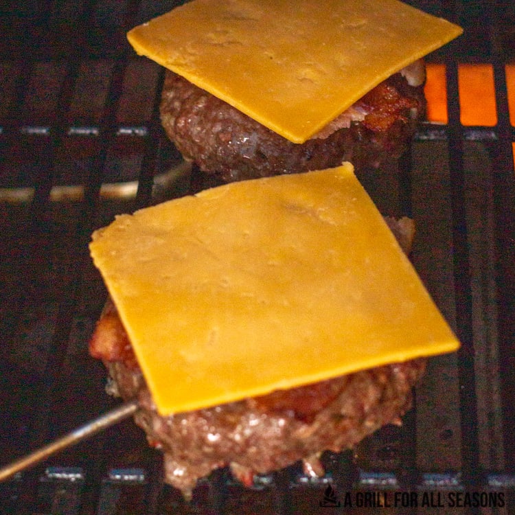 Burgers on Traeger grill topped with bacon and cheddar slices.