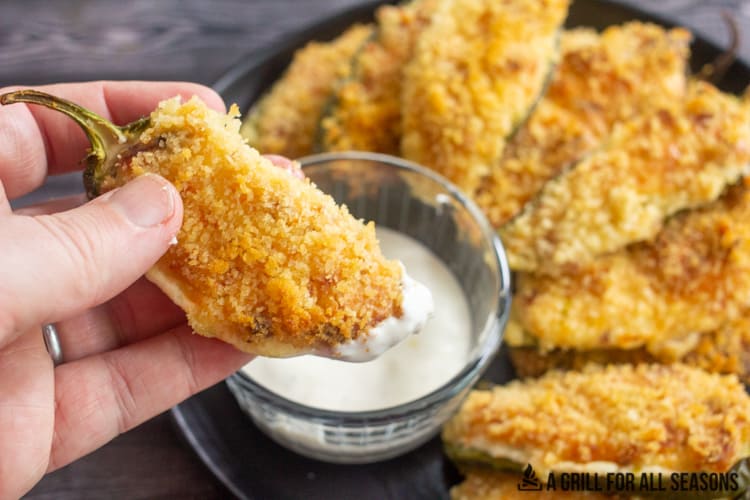 Smoked jalapeno poppers on plate with ranch dressing for dipping with one pooper being dipped.