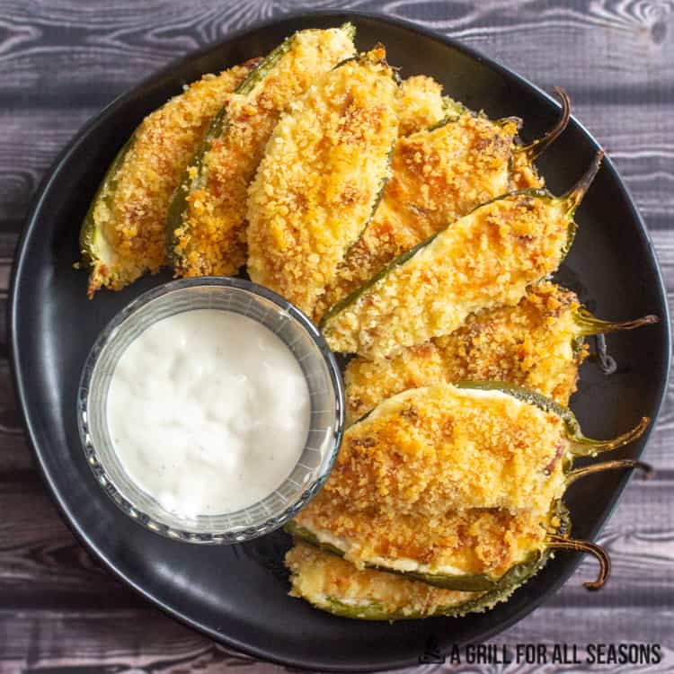 Smoked jalapeno poppers on plate with ranch dressing for dipping.
