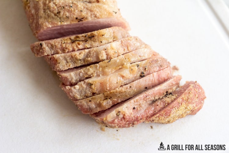 Smoked pork tenderloin sliced on cutting board.