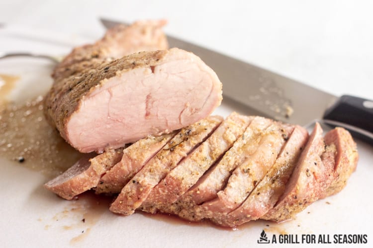 Smoked pork tenderloin sliced on cutting board.