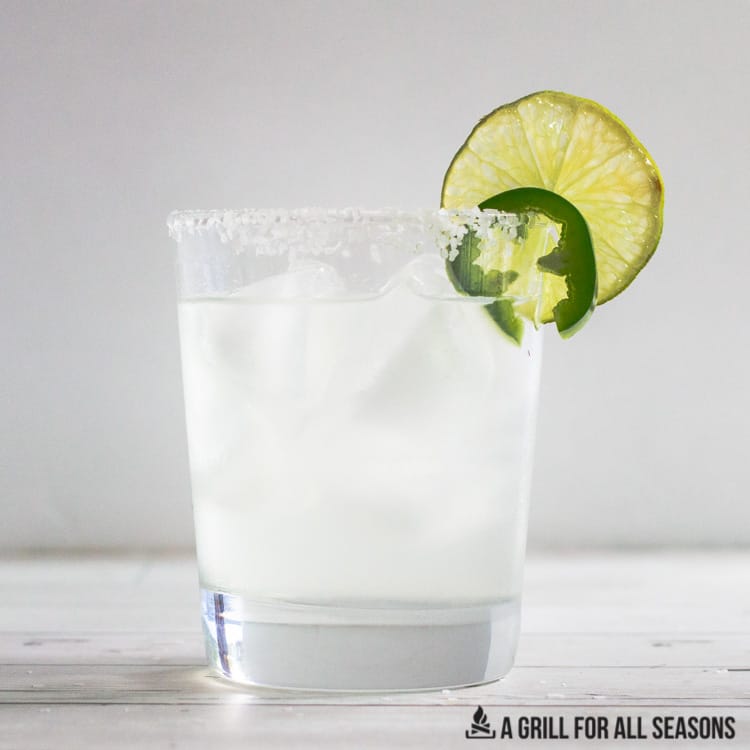 spicy skinny margarita in a rocks glass garnished with a lime and jalapeno slice.