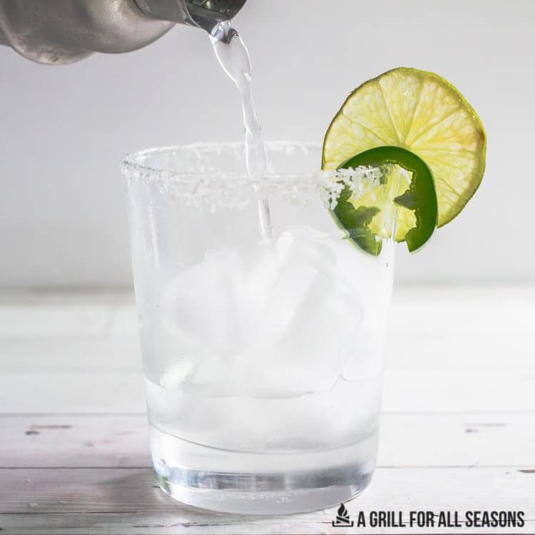 spicy skinny margarita pouring into a rocks glass garnished with a lime and jalapeno slice.
