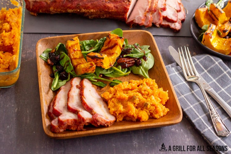 serving plate with smoked traeger pork loin slices, mashed sweet potatoes, and salad.