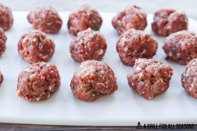 Fifteen venison meatballs raw, sitting on cutting board.