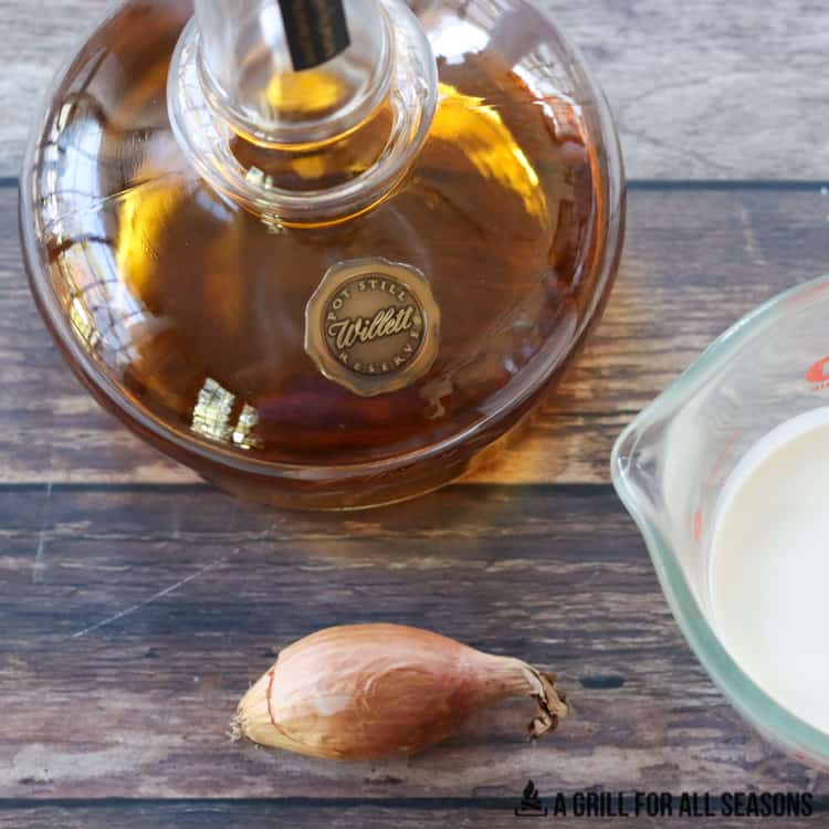 Whole Shallot, measuring cup with heavy cream. Bottle of bourbon.