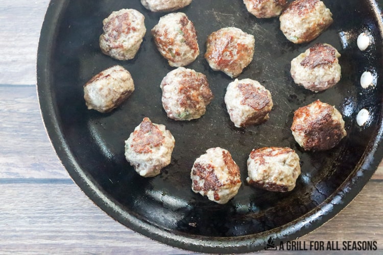 Venison meatballs being seared in frying pan.