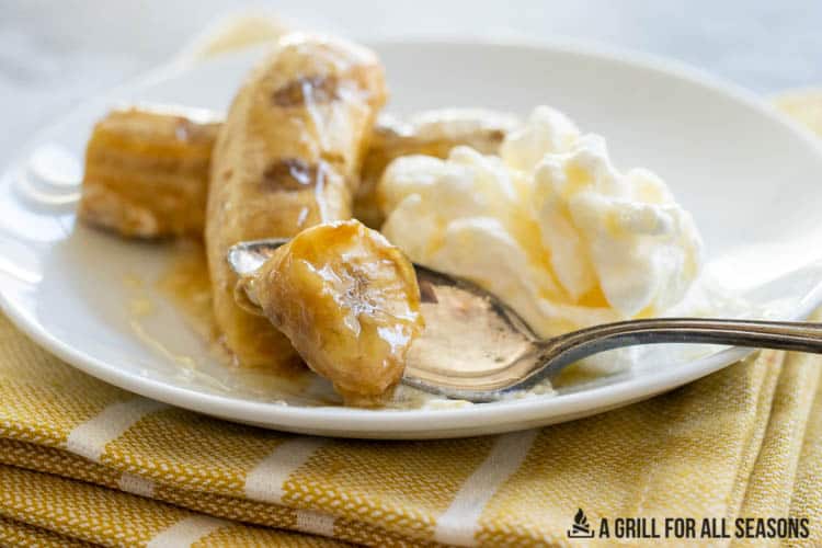 bite of banana on spoon on plate with whipped cream and caramel