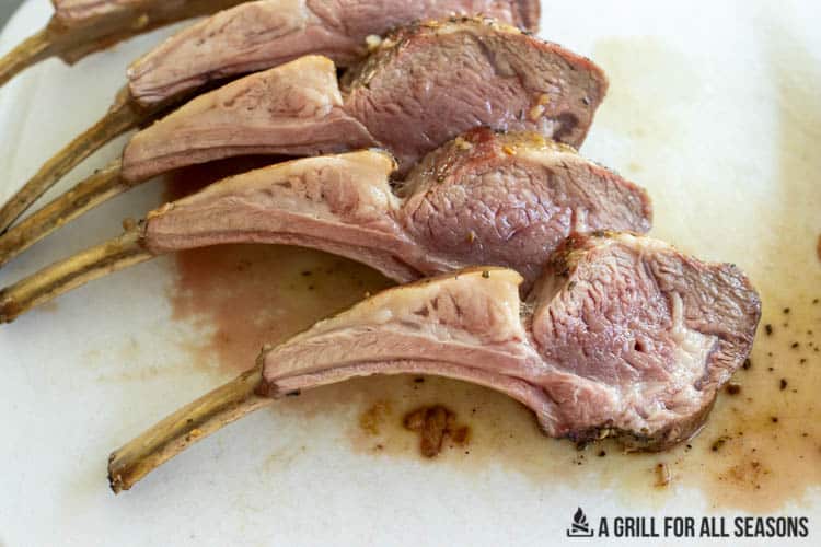 Smoked rack of lamb cut into five chops sitting on cutting board.