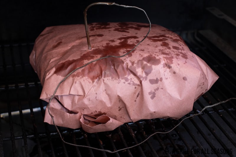 Pork wrapped in pink butcher paper cooking on smoker.