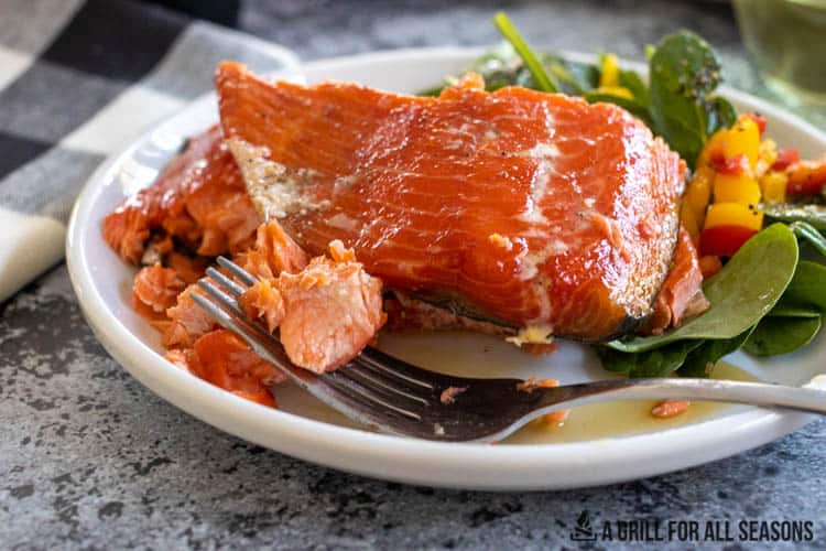 Smoked salmon fillet on plate with salad and fork holding a piece of salmon.