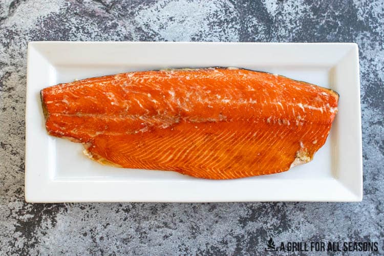 Smoked whole salmon fillet on white serving plater.