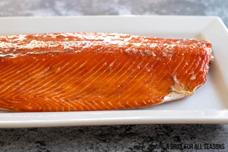 Smoked whole salmon fillet on white serving plater.