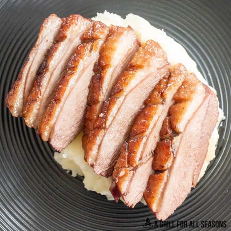Sliced smoked duck breast on a bed of mashed potatoes on a plate.