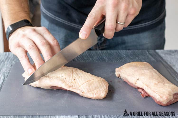 Scoring skin side of duck breast with sharp knife.