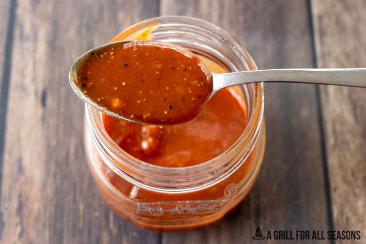 spoon with hot honey barbecue sauce resting on jar