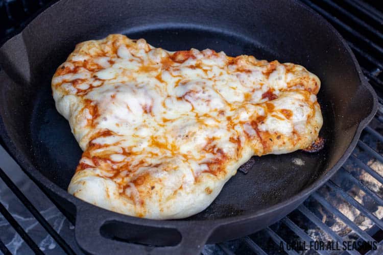 cast iron pan on grill with sauce and cheese covered dough