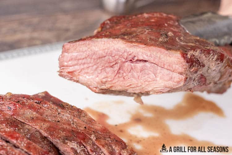 tongs holding up cut tri tip to show inside