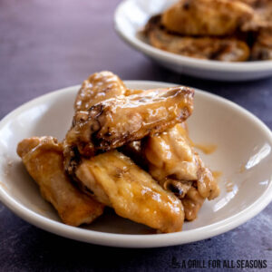 Traeger smoked chicken wings on a plate in sauce with more smoked chicken wings in background