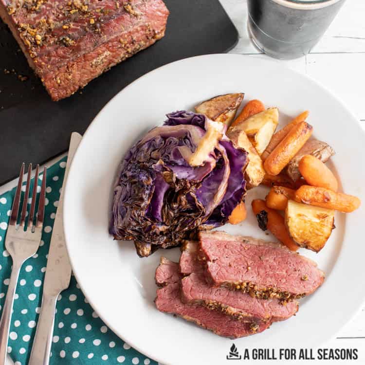 slices of traeger smoked corned beef on a plate with cabbage potatoes and carrots