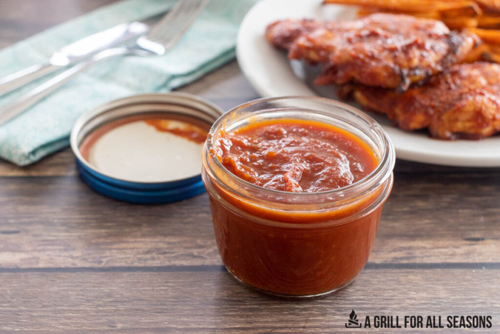 jar of barbecue sauce in front of plate with bbq chicken