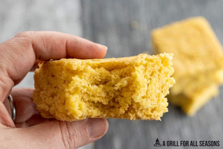 hand holding smoked cornbread with a bite missing