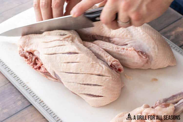 hands scoring the skin and fat of the whole duck with a knife