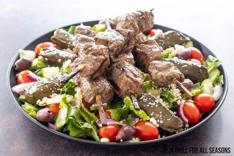 greek salad topped with beef kabobs