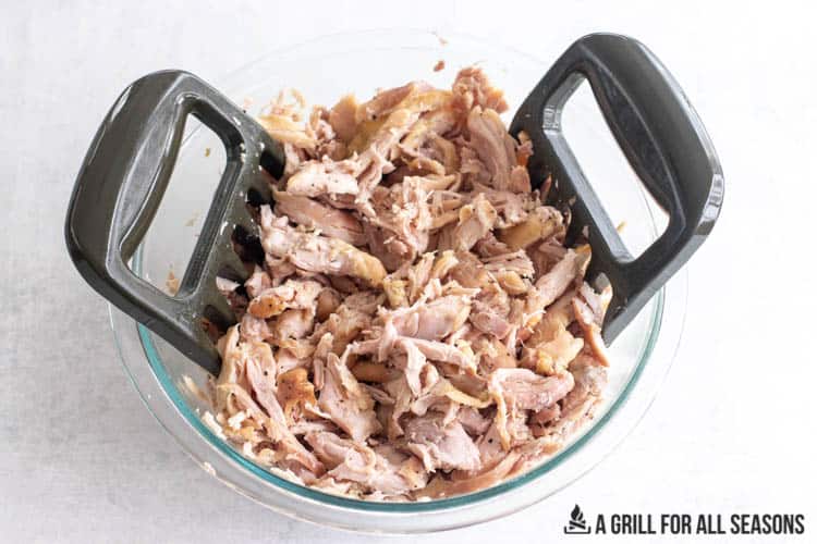 two shredding claws in bowl of smoked pulled chicken